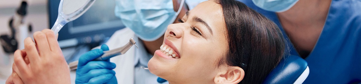 a patient looking at her smile in a mirror while sitting in a dental chair