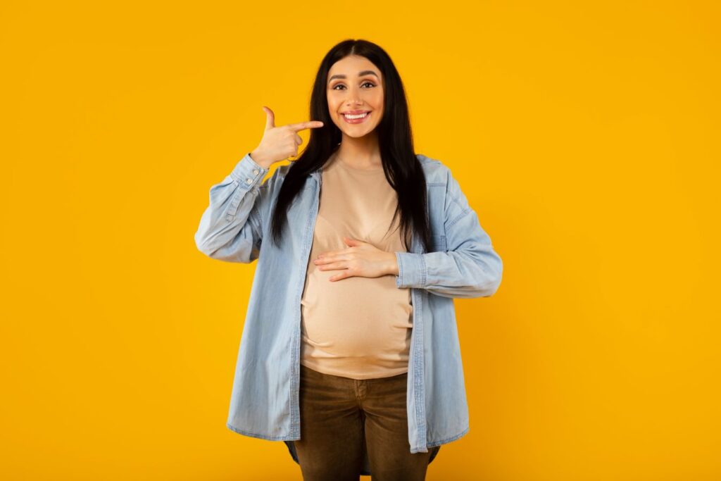 A pregnant woman pointing to her smile