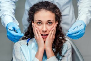 Patient in dentist’s chair expressing shock with hands clamped to sides of her face.